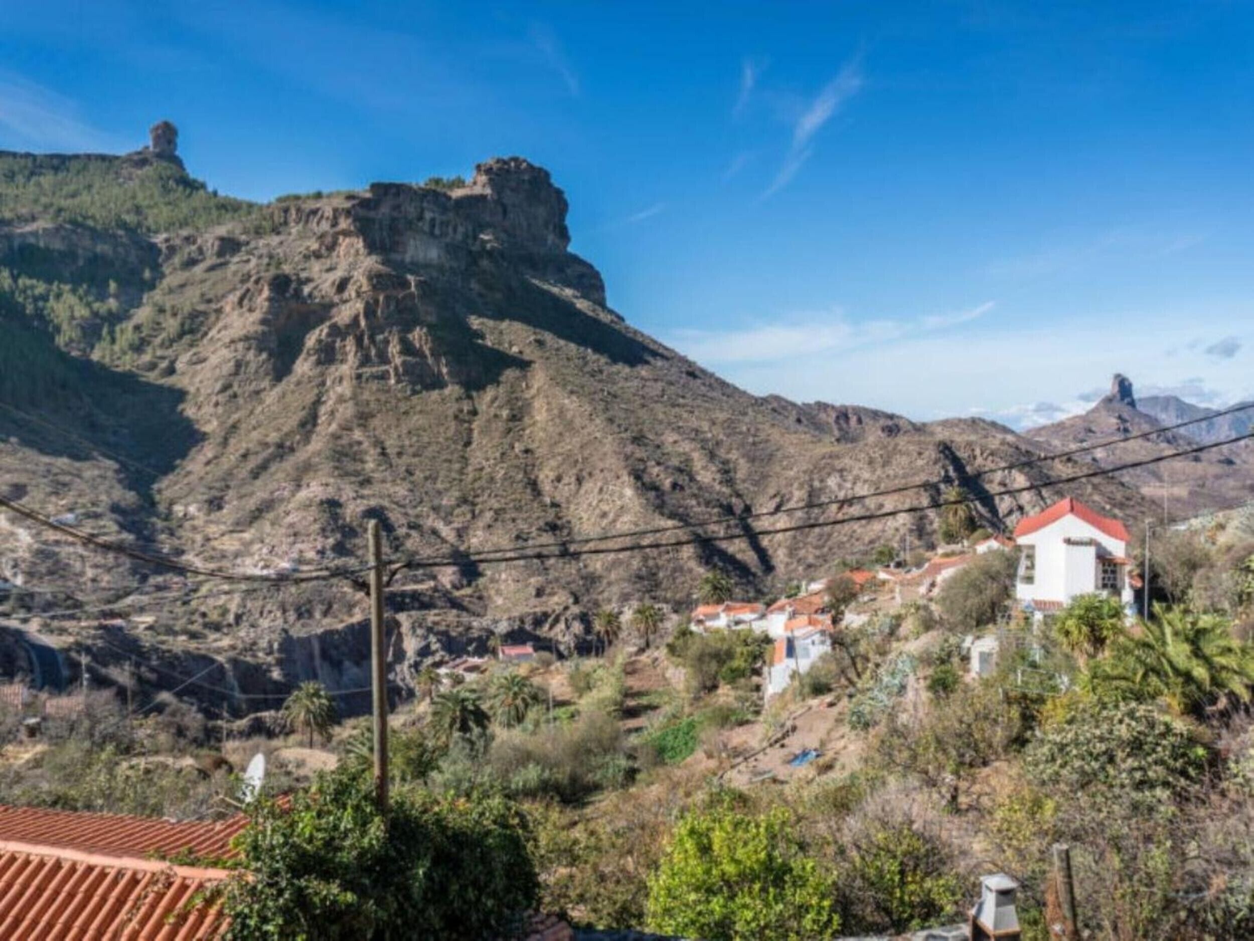A mountainous landscape with a prominent rocky peak and a small settlement with red-roofed buildings.