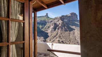 A room with a wooden ceiling, a window with curtains, and a view of a rocky mountain.