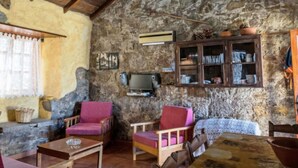 A rustic room with stone walls, wooden beams, a stone fireplace, a television, and a cabinet with dishes. - Casa Rural Pepita - Gran Canaria Center - Tejeda (Pagos de Casas Juan Gómez)