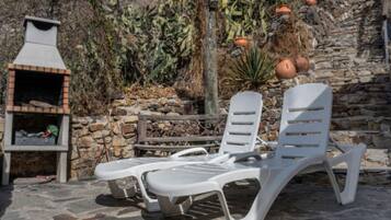 A stone wall, a barbecue grill, and two white lounge chairs.
