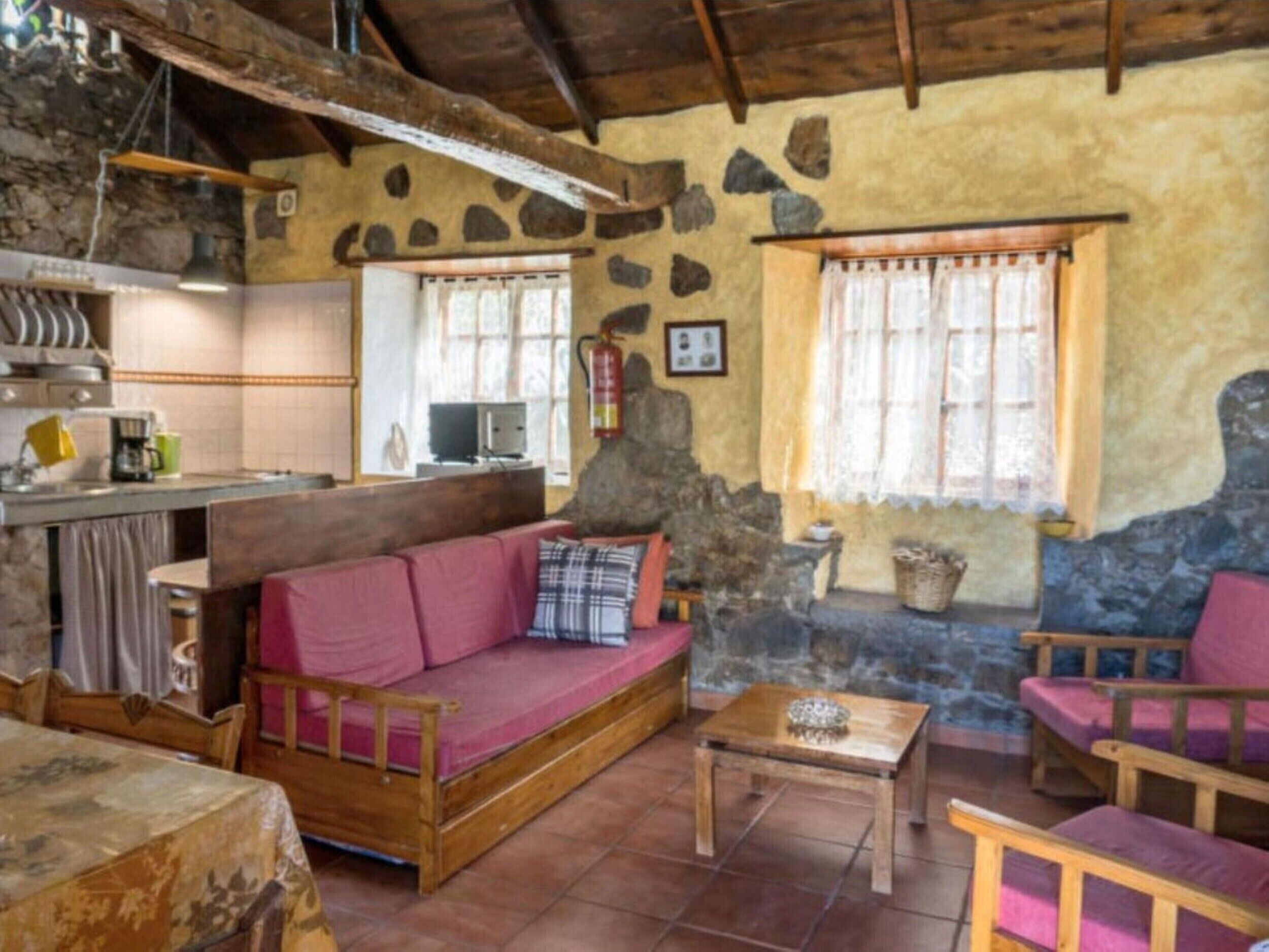 Un intérieur rustique avec un mur en pierre, des meubles en bois, un canapé, une petite table et un coin cuisine.
