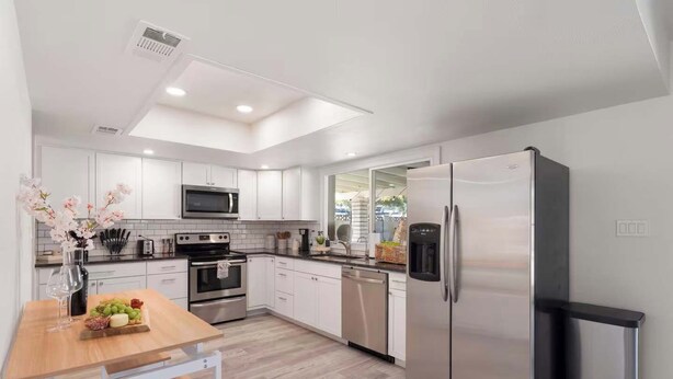 Una cocina moderna con armarios blancos, electrodomésticos de acero inoxidable y una mesa de comedor de madera.