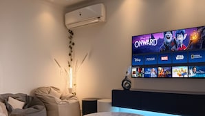 Un saló modern amb un televisor de pantalla plana gran que mostra una pel·lícula, un sofà, una taula de centre i un aparell d'aire condicionat.