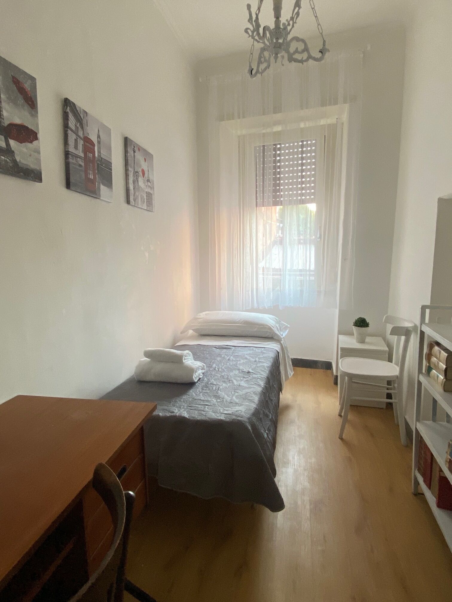 A small, tidy room with a bed, a desk, a chair, and a bookshelf.