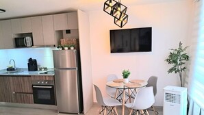A modern kitchen with stainless steel appliances, a dining area with a round table and chairs, and a flat-screen TV mounted on the wall. - New Studio apartment with AC, in front of train station Franklin, Santiago City. (Santiago)