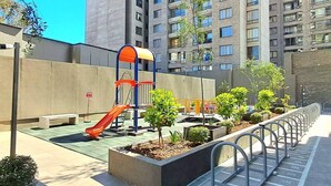 A playground with a slide and climbing structure, surrounded by a low wall and small trees. - New Studio apartment with AC, in front of train station Franklin, Santiago City. (Santiago)