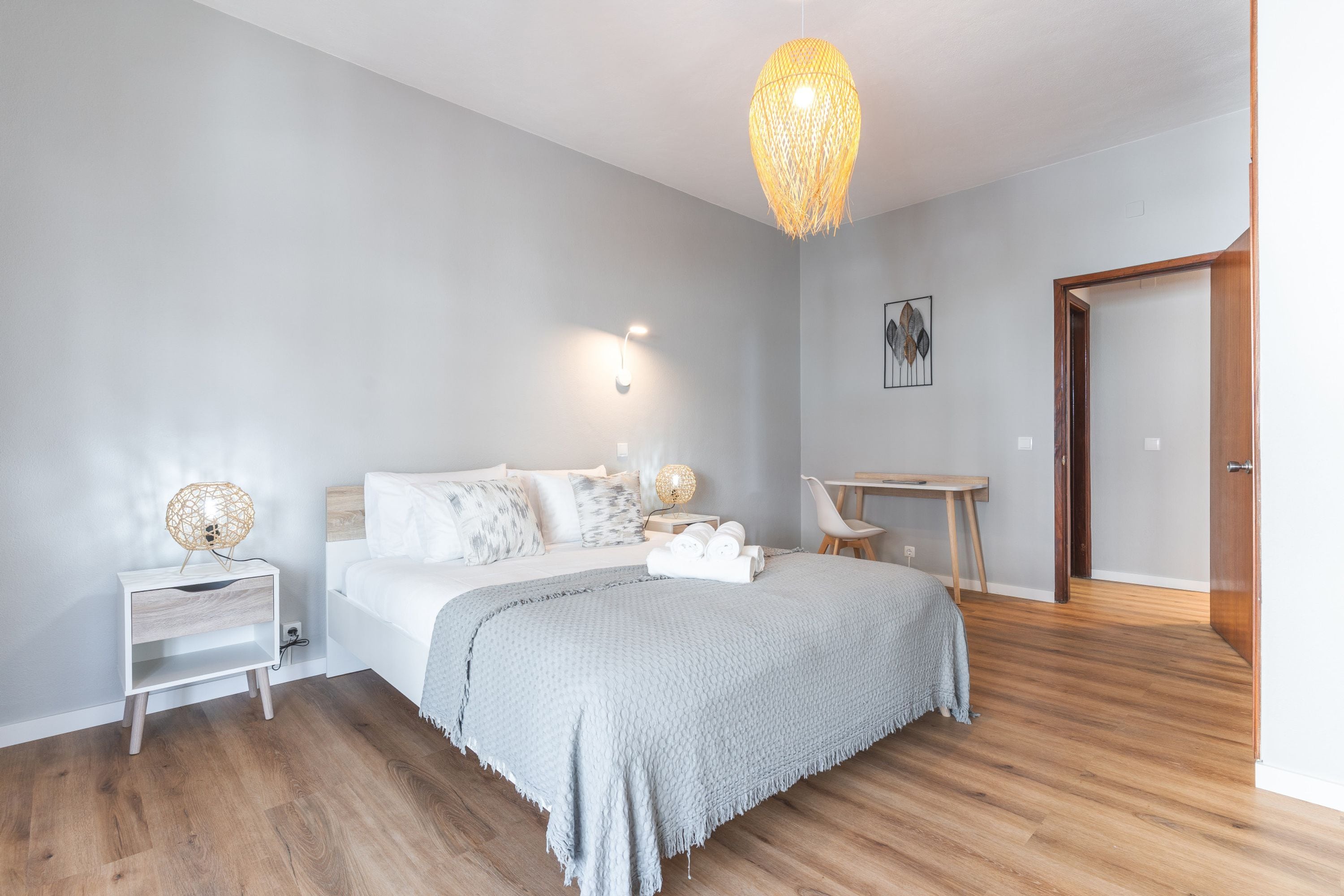 A modern bedroom with a large bed, bedside lamps, a desk, and a door.