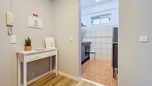 Un pasillo estrecho con piso de madera que conduce a una cocina con paredes de azulejos y una ventana.
