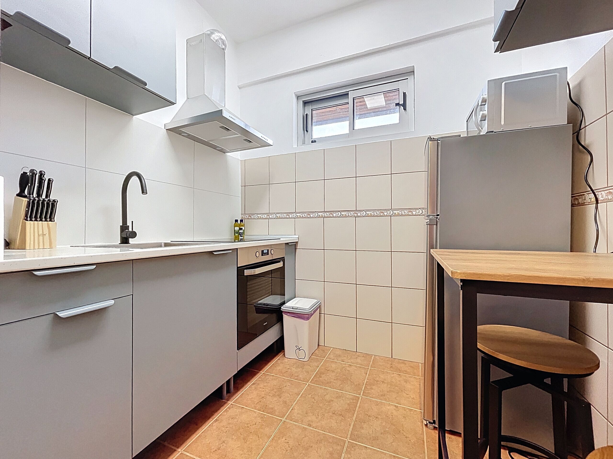 A modern kitchen with white cabinets, a stainless steel range hood, a built-in oven, and a small window above the sink.