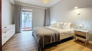 Un dormitorio con cama, mesita de noche, lámpara y vistas al exterior por una puerta corredera.