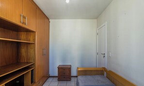 A small, compact room with a bed, a wooden wardrobe, and a small dresser. - Apt in Downtown BC 350m From the Beach Pae1002 (Balneário Camboriú)