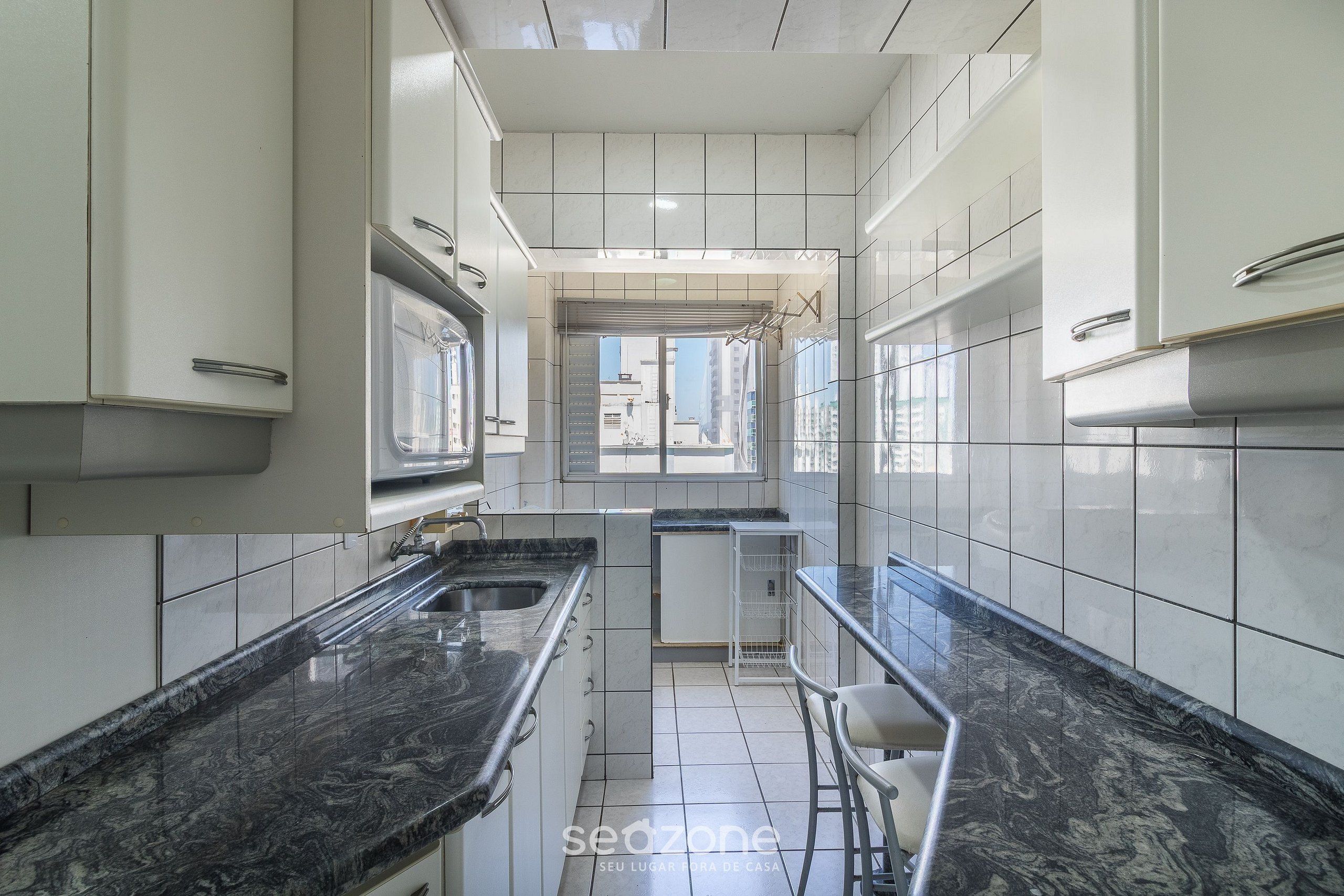 Una cocina moderna con armarios blancos, encimeras de mármol negro y una pequeña isla con taburetes.