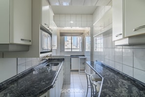 A modern kitchen with white cabinets, black marble countertops, and a small island with bar stools. - Apt in Downtown BC 350m From the Beach Pae1002 (Balneário Camboriú)