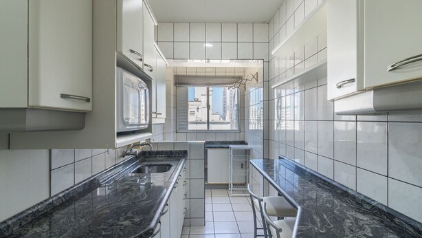 A modern kitchen with white cabinets, black marble countertops, and a small island with bar stools. - Apt in Downtown BC 350m From the Beach Pae1002 (Balneário Camboriú)
