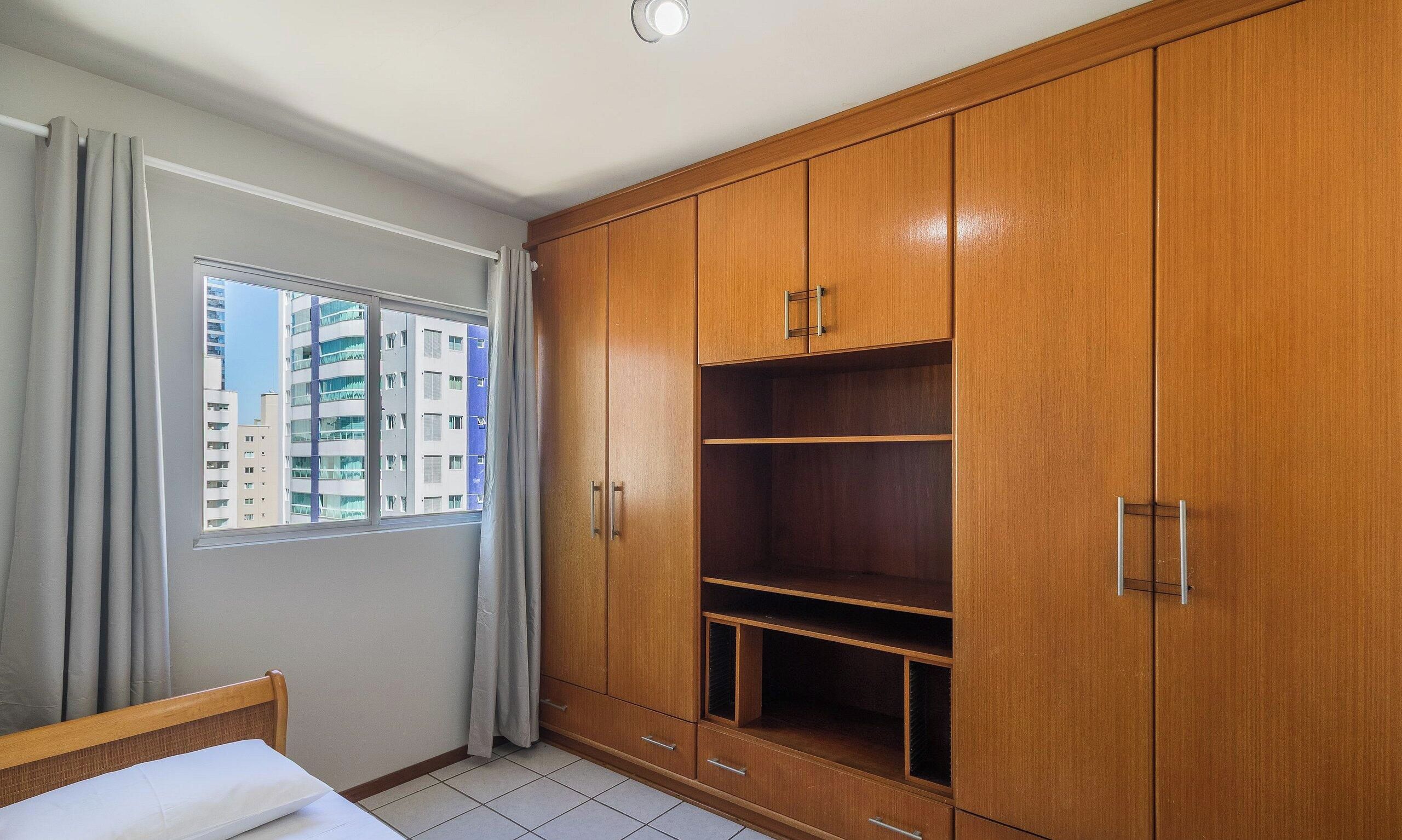 Un dormitorio con cama, ventana con cortinas y un armario de madera con varios compartimentos.