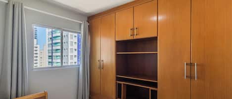 A bedroom with a bed, a window with curtains, and a wooden wardrobe with multiple compartments.