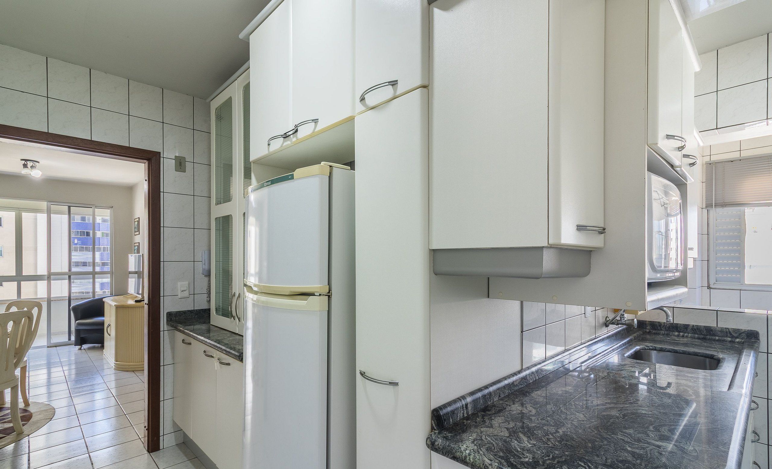 Una cocina con armarios blancos, un refrigerador y una encimera de granito.