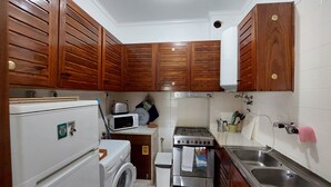 Une cuisine compacte dotée de meubles en bois, d’un lave-linge, d’un four à micro-ondes, d’une cuisinière à gaz et d’un évier.