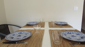 Una mesa de comedor con manteles individuales, platos, vasos y cubiertos.