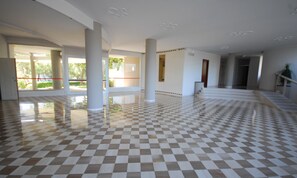 Eine großzügige Lobby mit Schachbrettmuster-Boden, großen Säulen und Blick ins Freie.