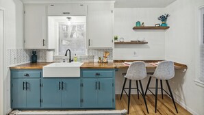 Una cocina con una isla central, dos taburetes de bar y una ventana con persianas.