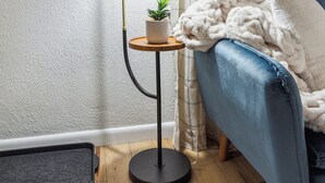 Una habitación acogedora con un sofá azul, una lámpara de pie, una pequeña planta en maceta y un adorno en la pared.