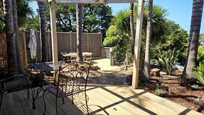 A covered patio area with a wooden deck, metal chairs, and a table. - Cedar Hill Retreat - great family property within easy reach of patrolled beach and shops (Venus Bay)