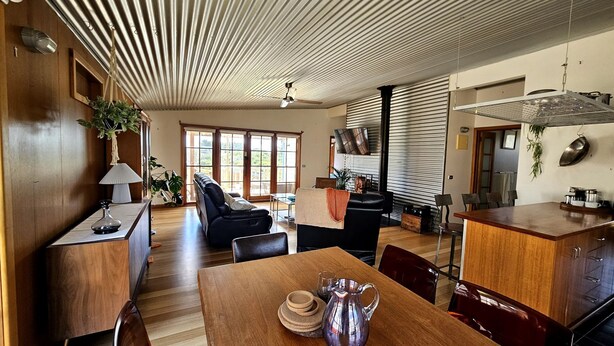 A spacious living area with a wooden dining table, a sofa, and a kitchen area with a grill. - Cedar Hill Retreat - great family property within easy reach of patrolled beach and shops (Venus Bay)