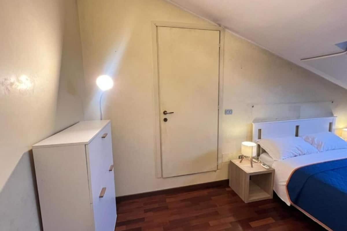 A bedroom with a bed, bedside table, lamp, and a wardrobe.