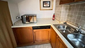 A compact kitchen with wooden cabinets, a dishwasher, a toaster, and a tiled backsplash. - Bergamoinhome (Bergamo)