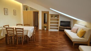 A dining area with a table and chairs, a sofa, a TV, and a bookshelf. - Bergamoinhome (Bergamo)