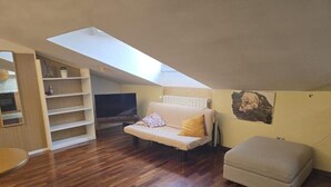 A cozy loft bedroom with a skylight, a sofa bed, a small ottoman, and a television. - Bergamoinhome (Bergamo)