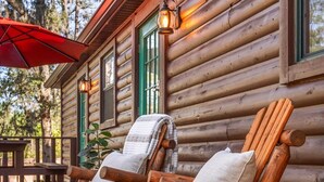 Une cabane en rondins avec deux fauteuils Adirondack en bois sur une véranda, un parasol rouge et une table en bois.