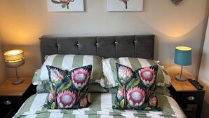 Una cama bien hecha con almohadas estampadas con flores, una colcha a rayas y dos cuadros con motivos florales en la pared.