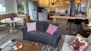 Una cocina moderna con una isla central, un comedor con una mesa redonda y una sala de estar con un sofá gris y almohadones decorativos.