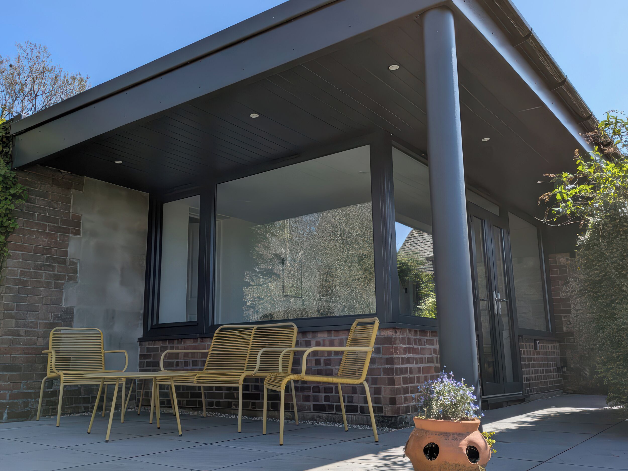A covered patio with a brick wall, large windows, and outdoor furniture.