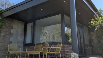A covered patio with a brick wall, large windows, and outdoor furniture.