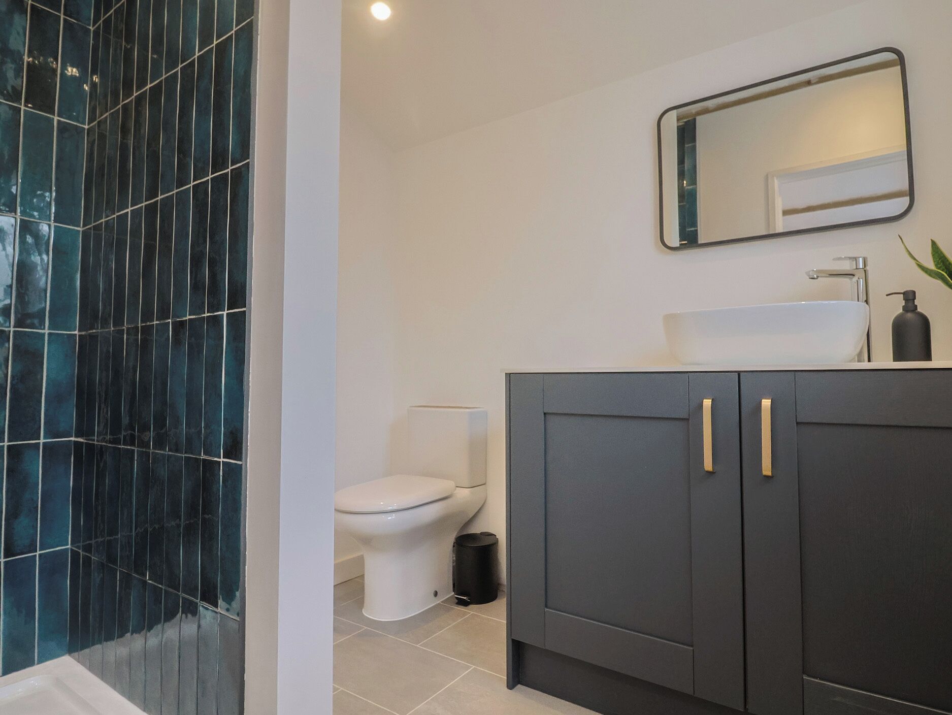 Une salle de bain moderne avec des toilettes blanches, des meubles de rangement gris foncé et un lavabo blanc.