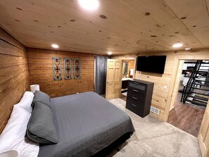 A wooden-paneled bedroom with a bed, dresser, and a flat-screen TV mounted on the wall.