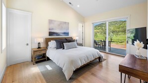 A bedroom with a large bed, a nightstand, a lamp, a ceiling fan, and a view of the outdoors through a sliding glass door. - Beautiful & dog-friendly vacation retreat in the heart of Sonoma Country (Santa Rosa)