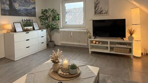 Un salon moderne avec un téléviseur à écran plat, une table à manger équipée d’une télécommande, une plante en pot et un tableau accroché au mur.