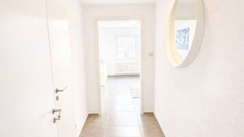 Un couloir avec une porte sur le côté gauche, un luminaire au plafond et un miroir sur le mur de droite.