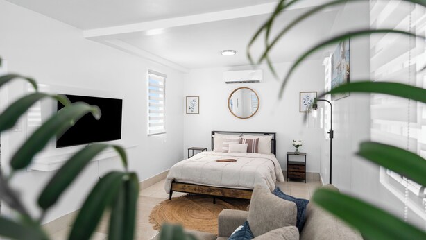 A bedroom with a bed, a TV, a bedside table, a mirror, and a window with blinds. - 63 Bay View by Otium (Catano)