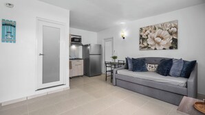 A modern apartment with a grey sofa, a dining table, a kitchen with a fridge, and a wall-mounted light fixture. - 63 Bay View by Otium (Catano)