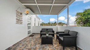 A covered outdoor seating area with wicker furniture, a wall-mounted plant, and a view of the surrounding landscape. - 63 Bay View by Otium (Catano)