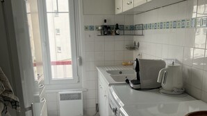 Una cocina compacta con armarios blancos, una estufa, un lavamanos y una ventana.