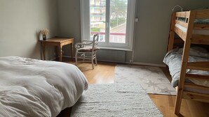 Un dormitorio con una cama individual superior e inferior, un escritorio, una silla y una ventana que ofrece vistas de edificios.