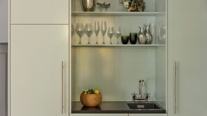 A kitchen with a wooden bowl of fruit, a sink, and wine glasses on shelves. - The Darling (Copenhagen)
