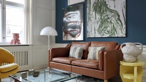 A room with a brown leather sofa, a glass coffee table, a yellow chair, and abstract art on the wall. - The Darling (Copenhagen)