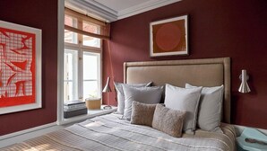 A bedroom with a large bed, a window with blinds, a framed artwork on the wall, and a bedside table. - The Darling (Copenhagen)